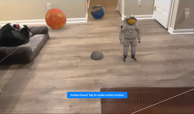 Augmented reality scene showing a small astronaut figure placed on a living room floor, with planets and a rock model visible and a surface detection message on screen.